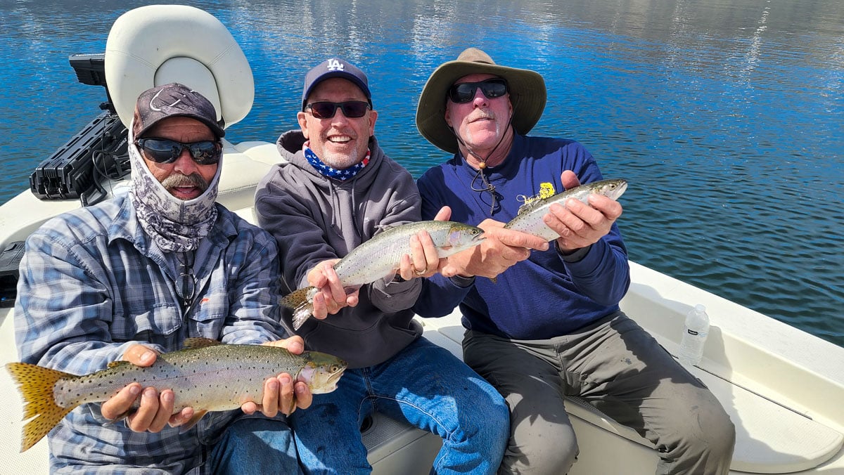 A trio of anglers holding 3 cutthroat trout in a boat on a lake.