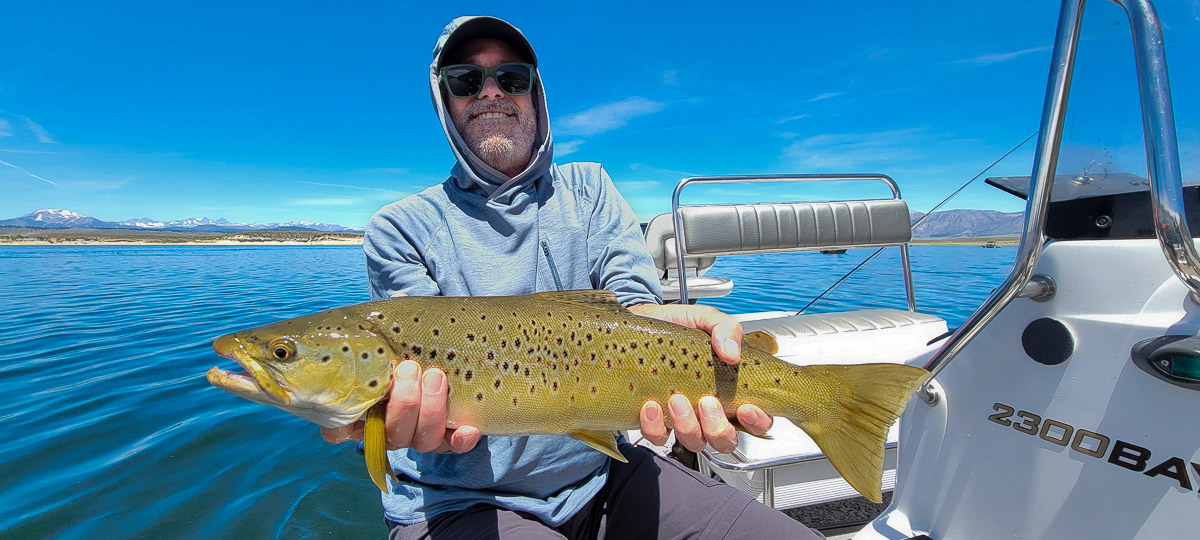 A fly fisherman on a lake in a boat holding a behemoth brown trout.