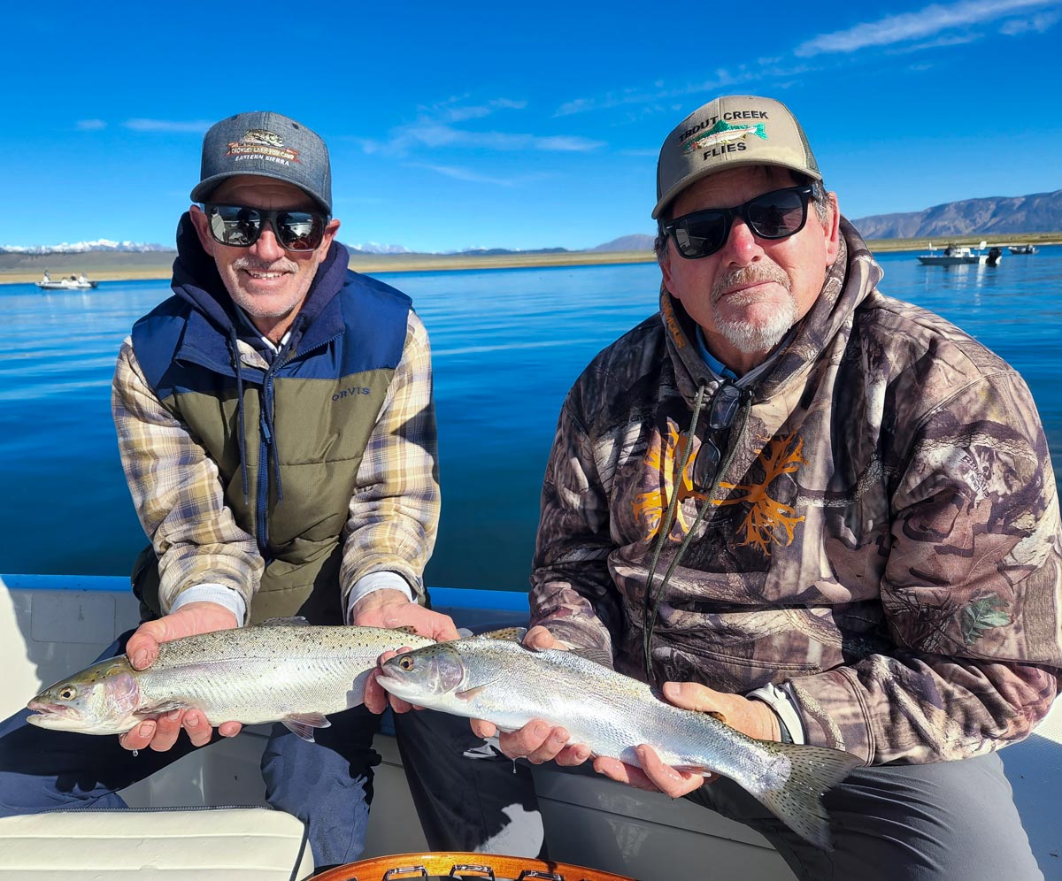 A pair of fly fishers on a lake in a boat holding a pair of nice rainbow trout.