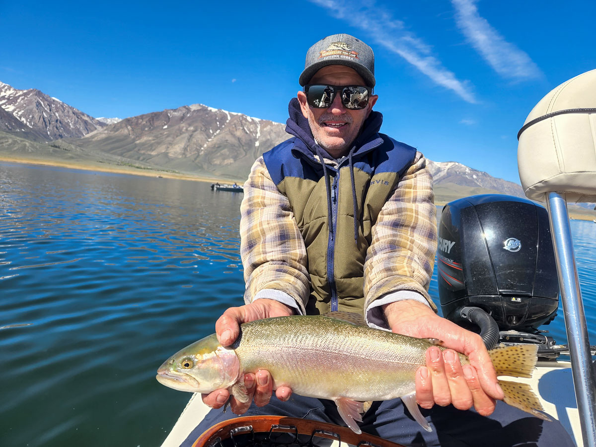 A fly fisherman in a boat holding a large cutthroat trout.