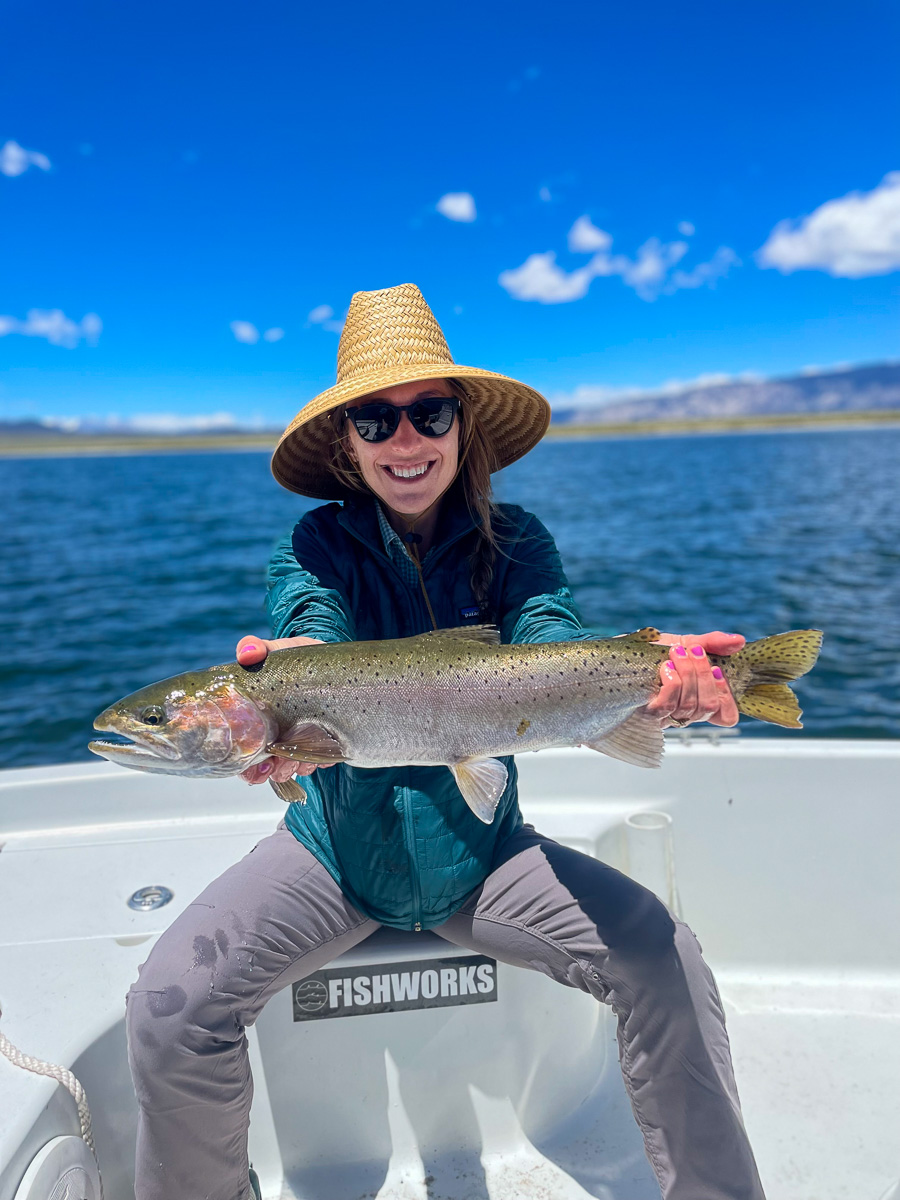 A female angler holding a large cutthroat trout in a boat on a lake.