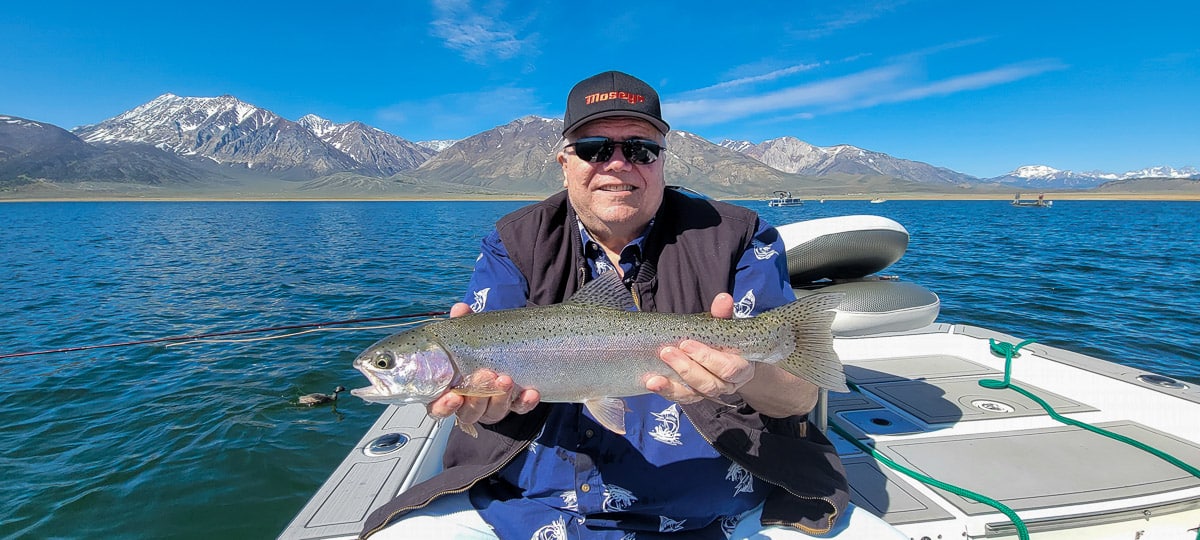 A fly fisherman on a lake in a boat holding a behemoth rainbow trout.