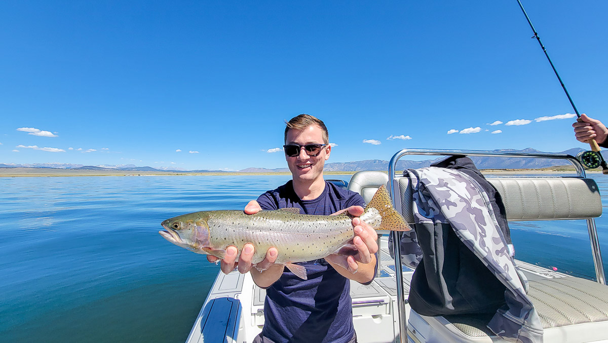 A fisherman holding a giant cutthroat trout on a boat in a lake.