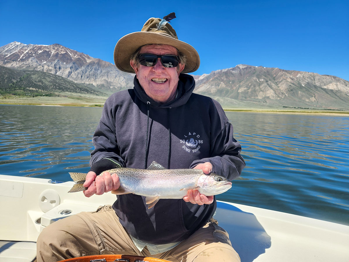 A smiling male angler holding a large rainbow trout in a boat on a lake.