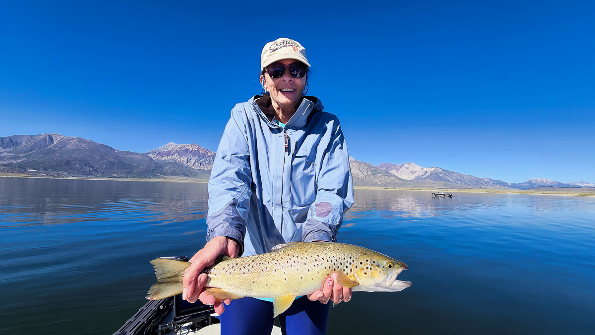 A fly fisherwoman on a lake in a boat holding a behemoth brown trout.