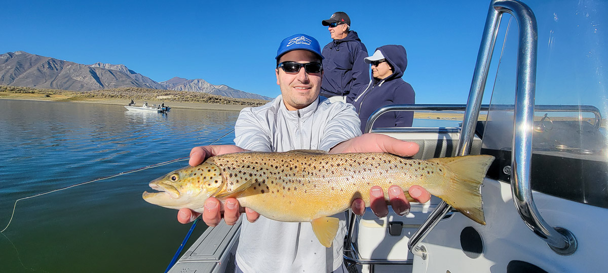 A smiling angler holding a giant brown trout on a lake..
