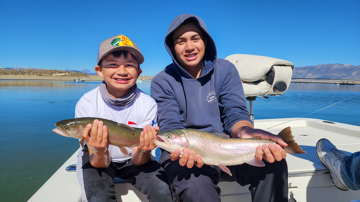 A pair of kids holding two large cutthroat trout in a boat.