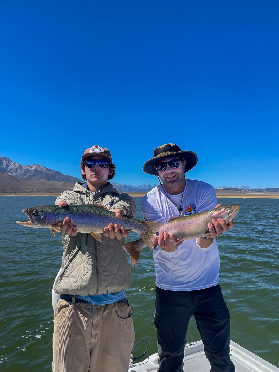 A smiling pair of fishermen holding a large rainbow and a large cutthroat trout.