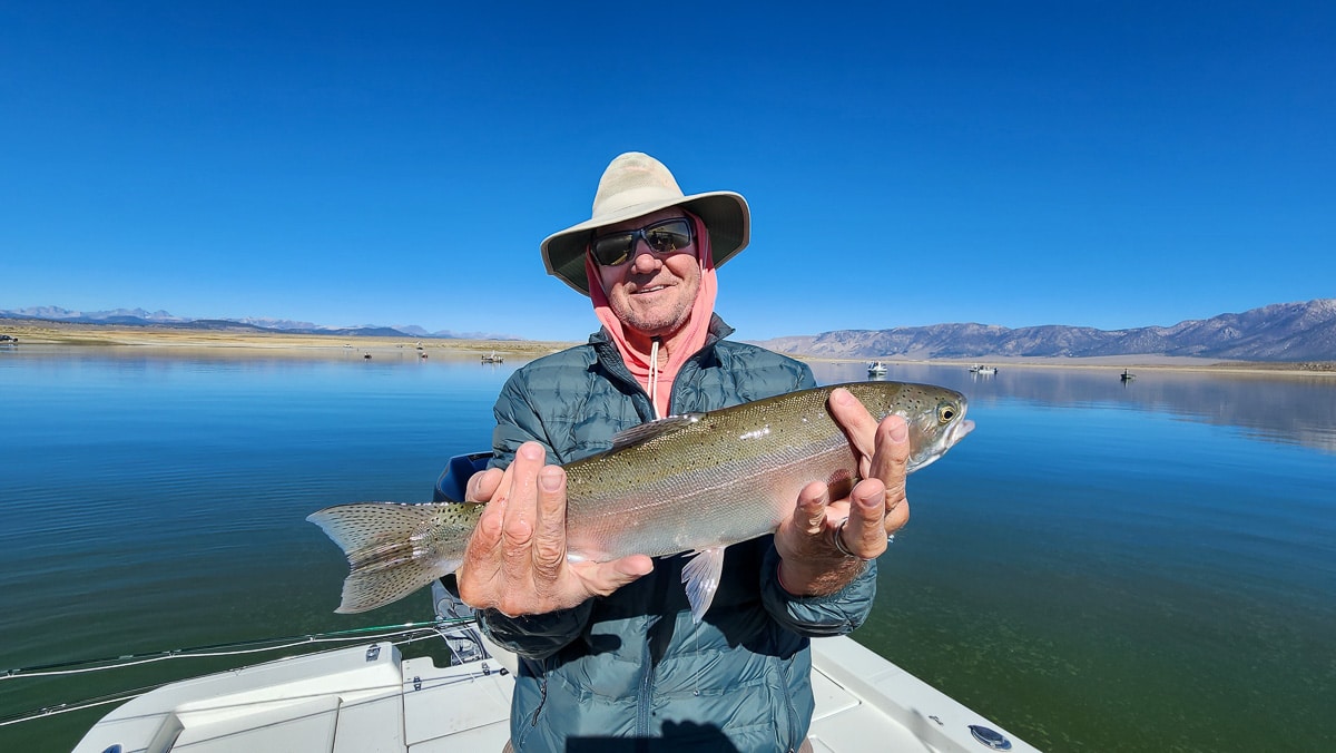 A fly fisherman on a lake in a boat holding a behemoth rainbow trout.