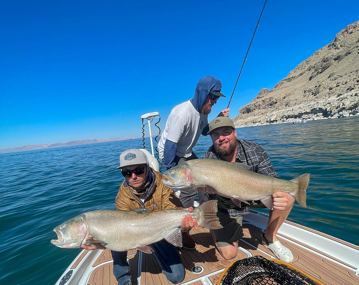 A pair of fishermen with monster sized cutthroat trout on a boat in a lake.