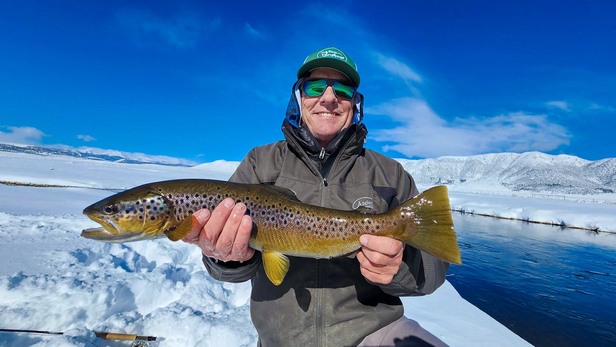 A fly fisherman holding a large brown trout.