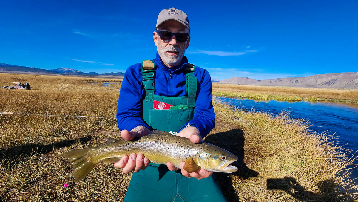 A fly fisherman holding a large brown trout.