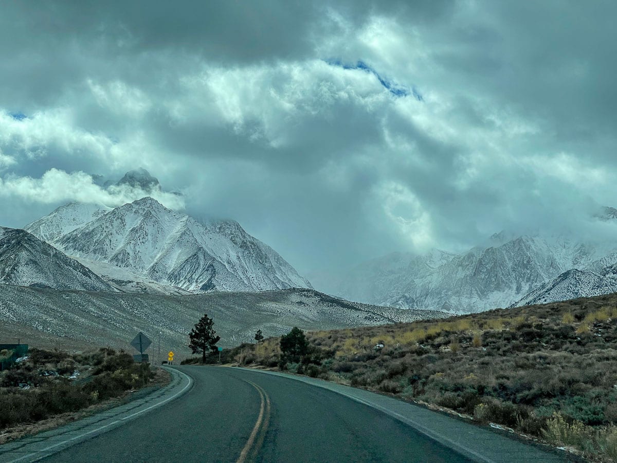 A snowstorm in the mountains from a two lane road.