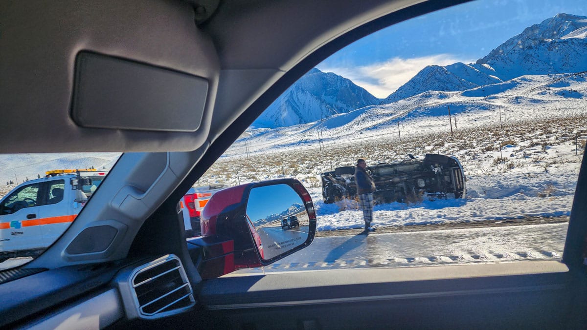 An overturned vehicle on the side of a highway in the snow.