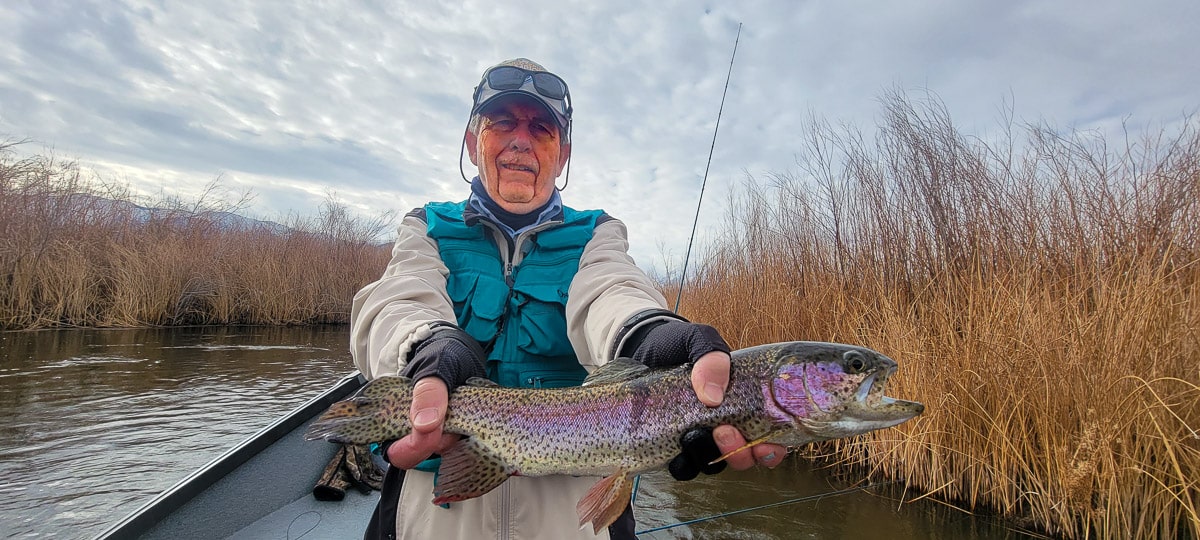 A smiling fisherman holding a rainbow trout in a river.