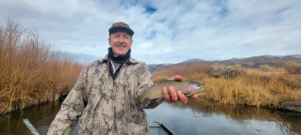 A smiling fisherman holding a rainbow trout in a river.