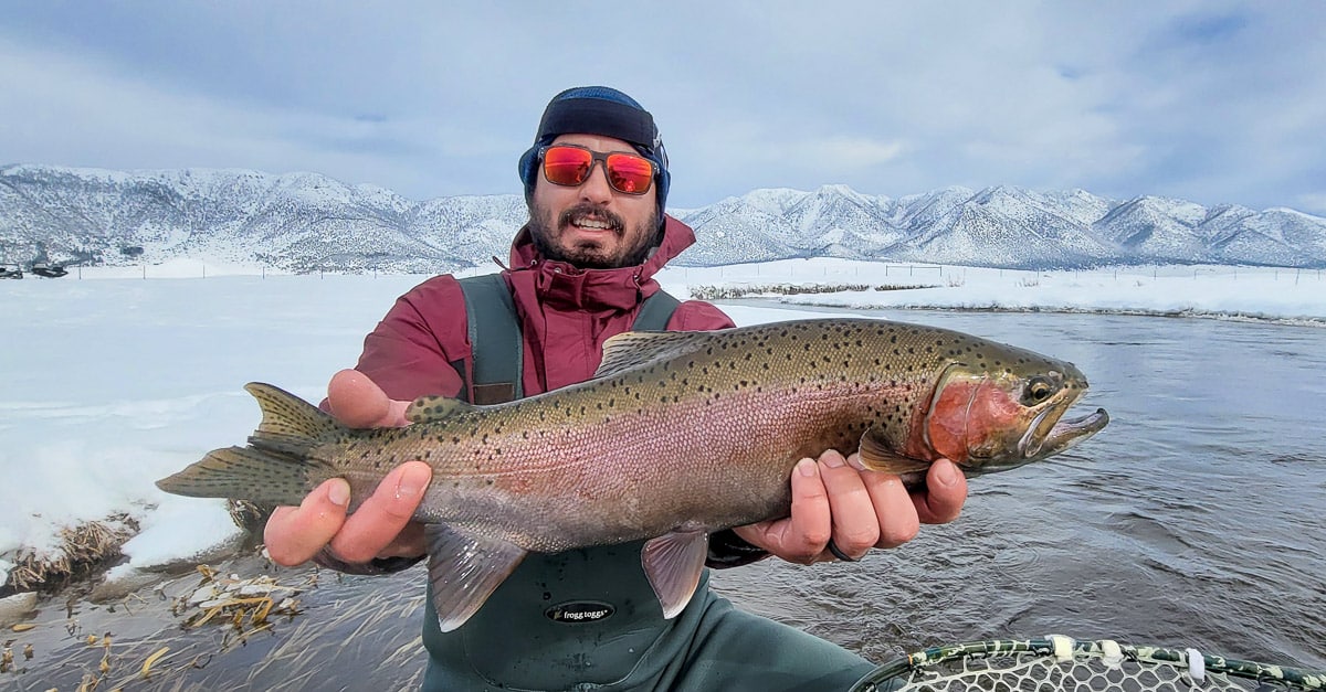 A smiling fisherman holding a rainbow trout in a river in the eastern sierra fishing zone.