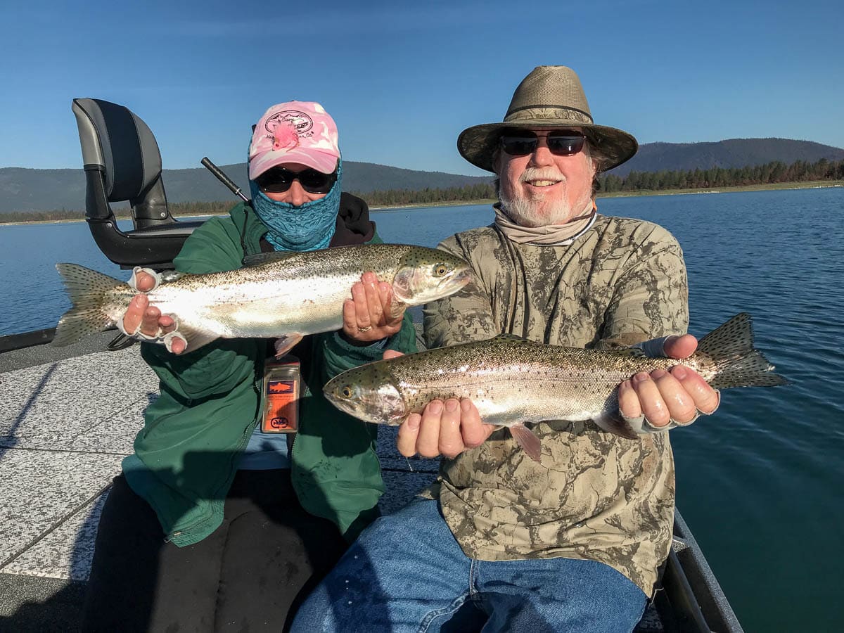 A man and a woman in a sun gaiter holding a pair of large rainbow trout in a boat on Eagle Lake.