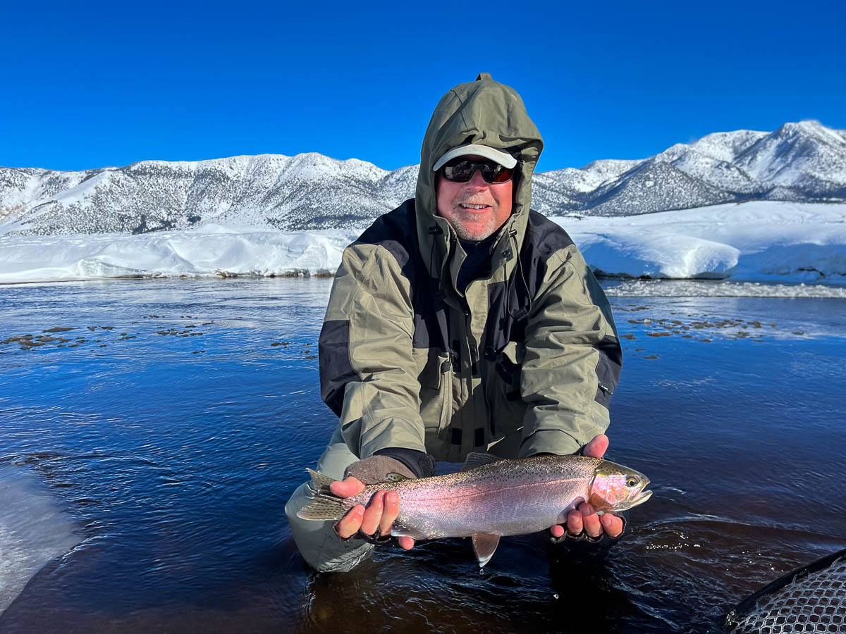 A smiling fisherman holding a rainbow trout in the Upper Owens River in the eastern sierra fishing zone.