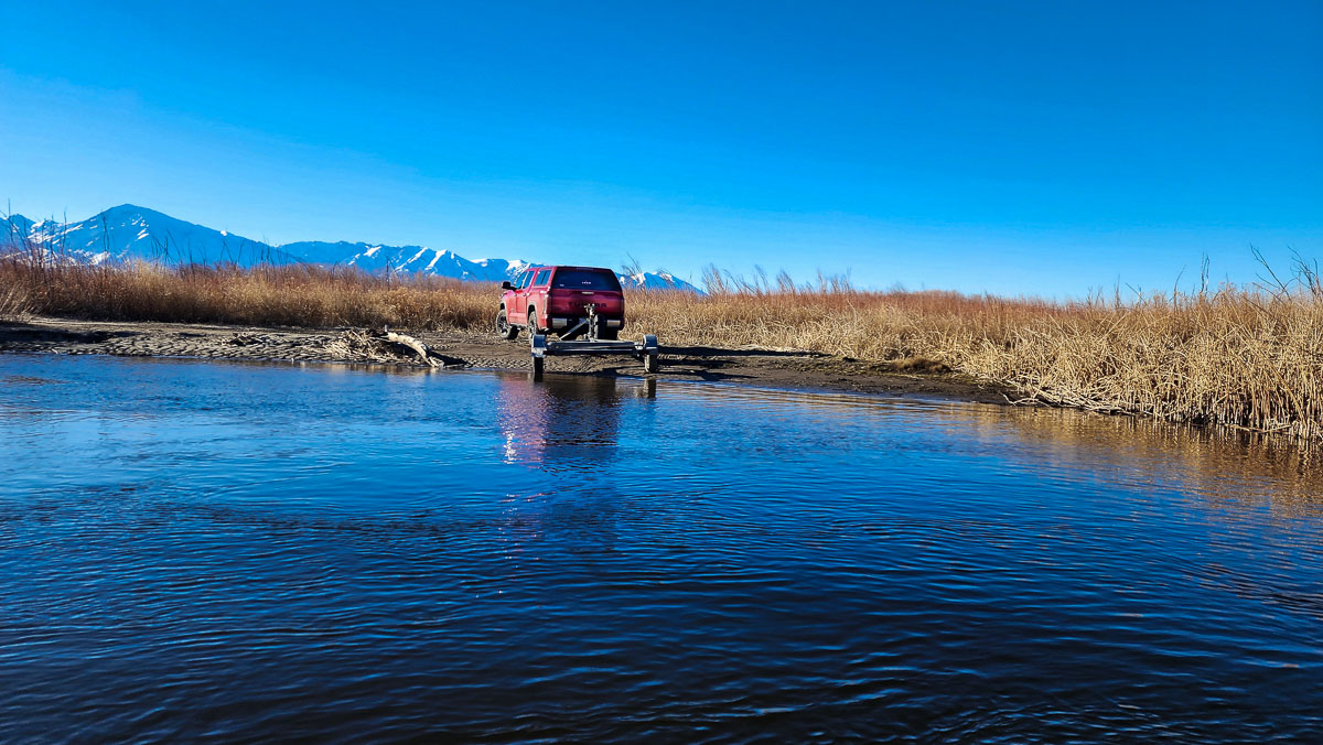 A red pickup truck parked on a river bank with a trailer attached.