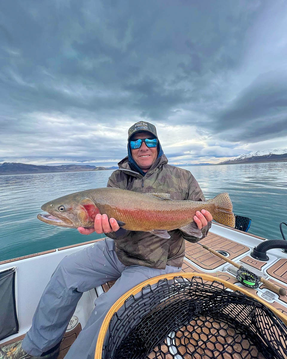 A fly fisherman holding a large cutthroat trout on a boat on Pyramid Lake.