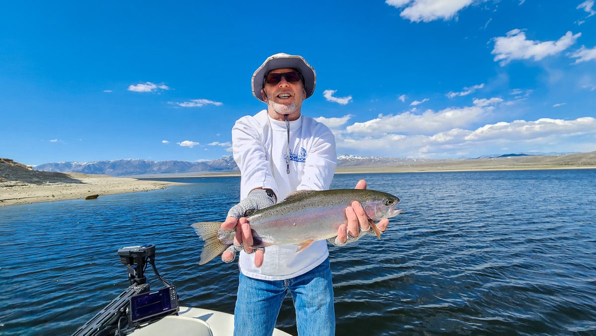 A fisherman holding a large rainbow trout from Crowley Lake on a boat.