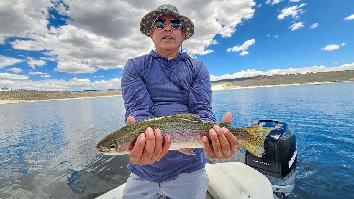 A fisherman holding a large rainbow trout from Crowley Lake on a boat.