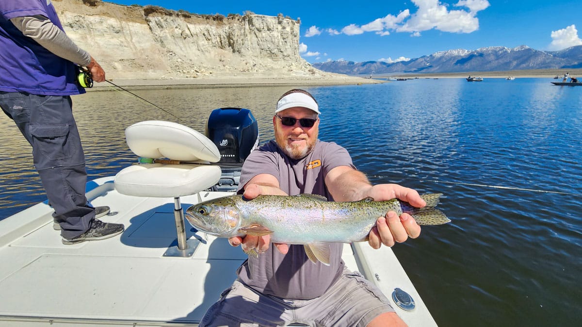 A fisherman holding a large rainbow trout from Crowley Lake on a boat.