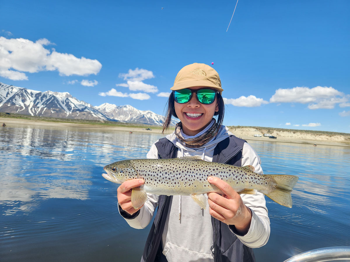 A young woman holding a large brown trout from Crowley Lake on a boat.