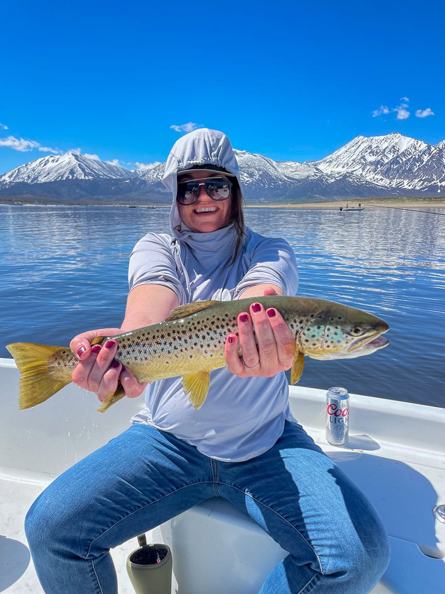 A young woman holding a large brown trout from Crowley Lake on a boat.