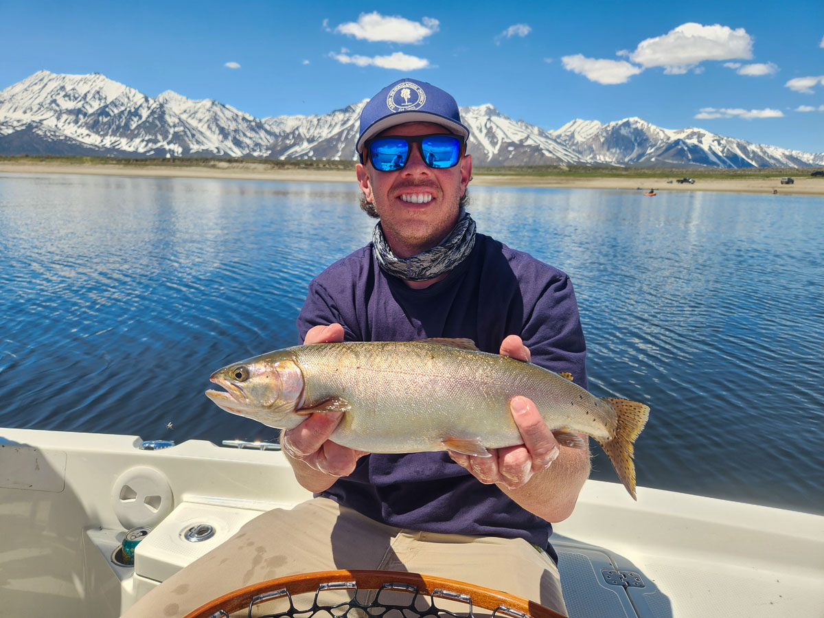 A young man holding a large cutthroat trout from Crowley Lake on a boat.