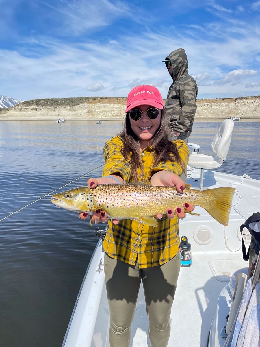 A young woman holding a large brown trout from Crowley Lake on a boat.