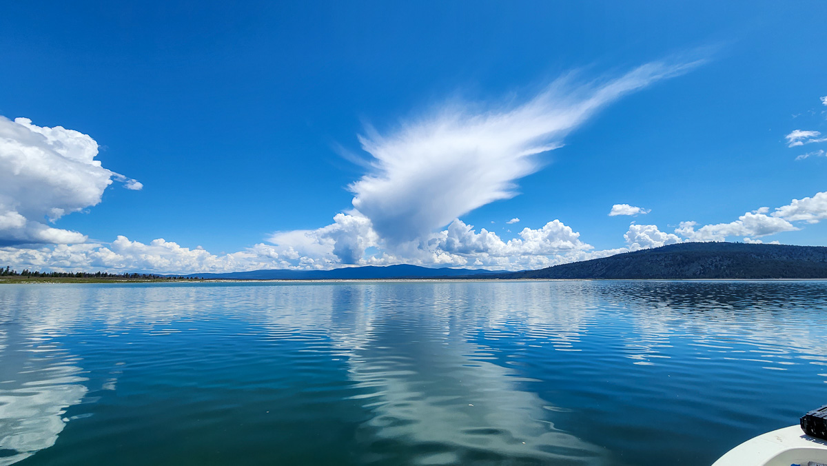 A big blue lake with mountains in the background and cumulus clouds in the sky.