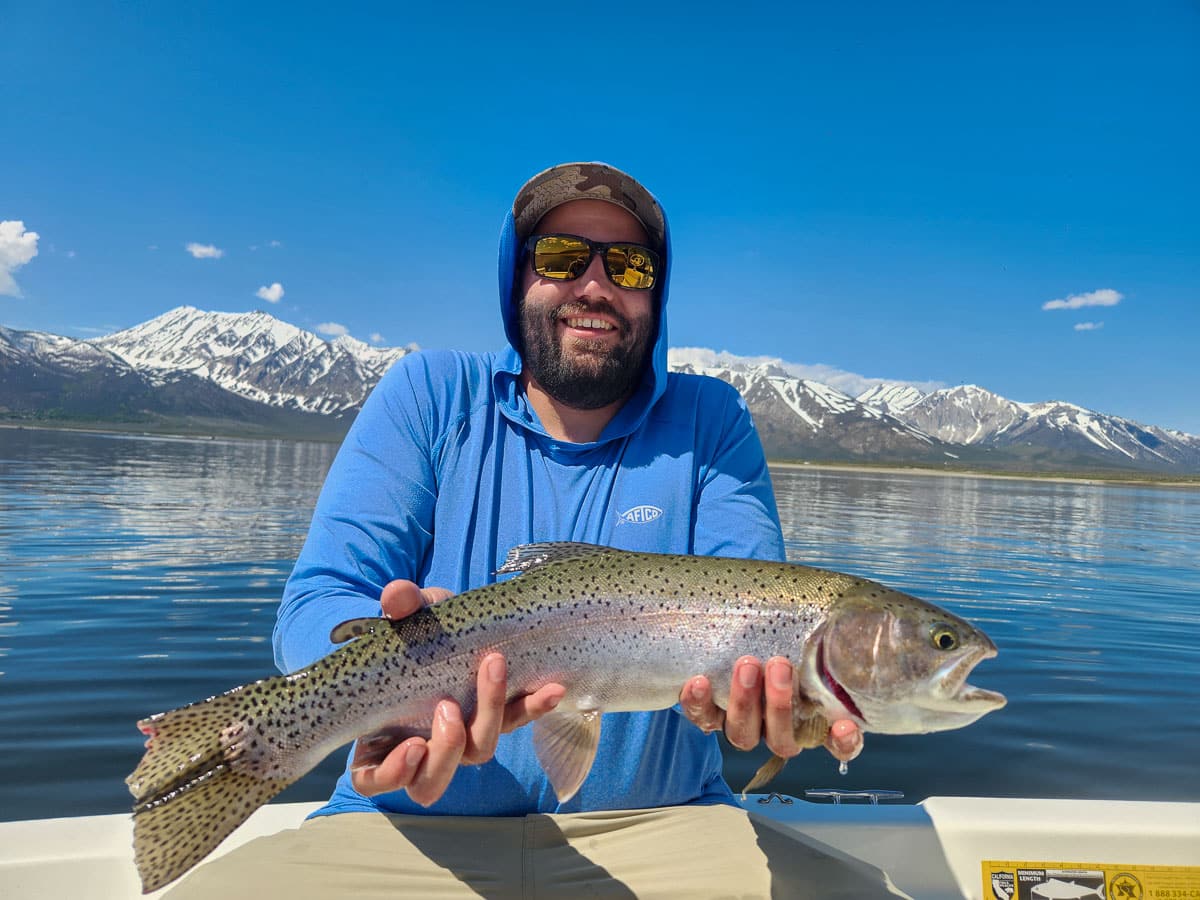 A fisherman holding a large rainbow trout from Crowley Lake on a boat.