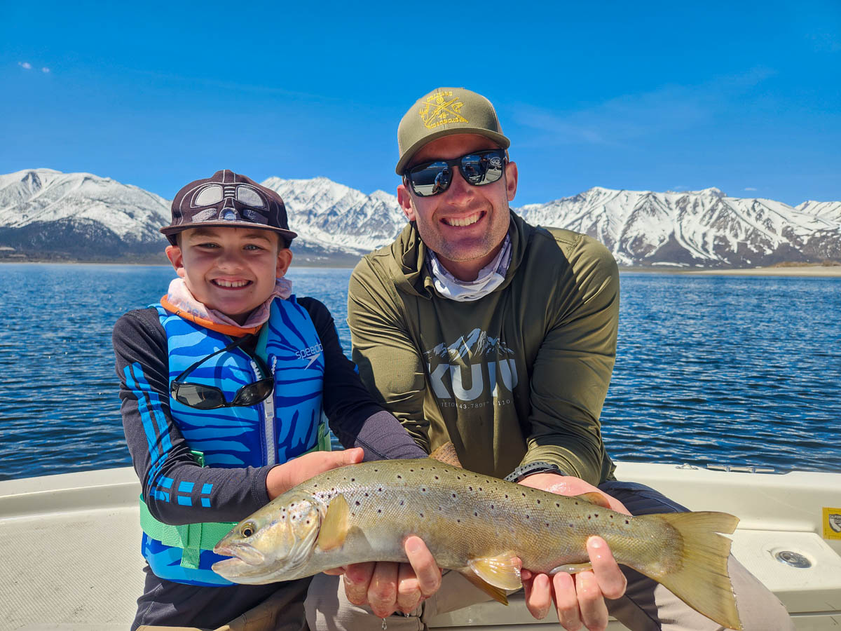 A man and a young boy holding a larger brown trout from Crowley Lake in a boat.