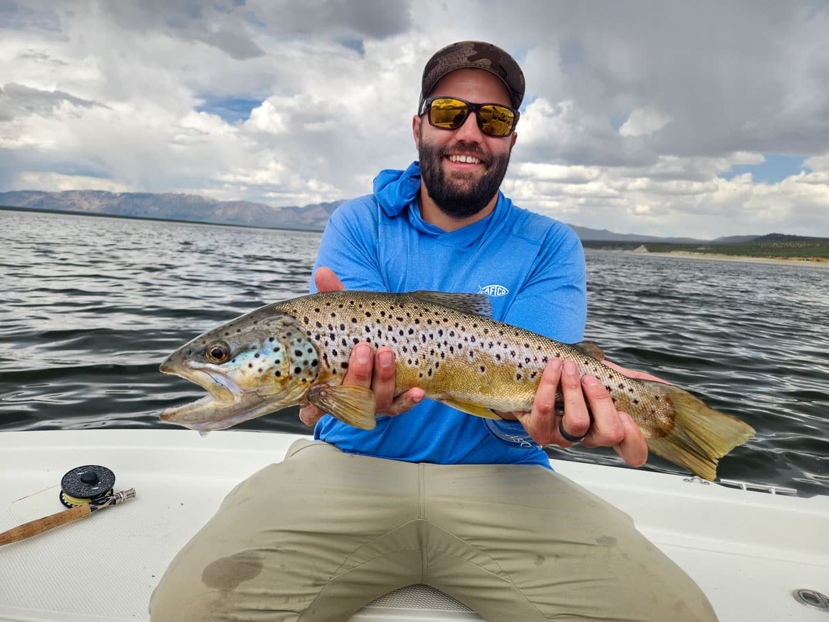 A fisherman holding a large brown trout from Crowley Lake on a boat.