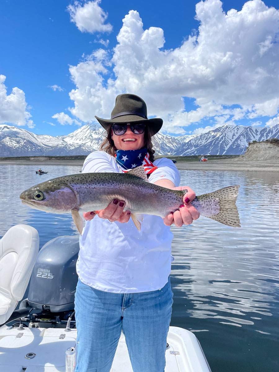 A young woman holding a large rainbow trout from Crowley Lake on a boat.