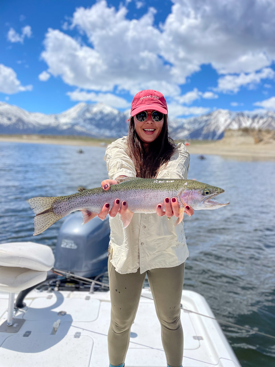 A young woman holding a large rainbow trout from Crowley Lake on a boat.