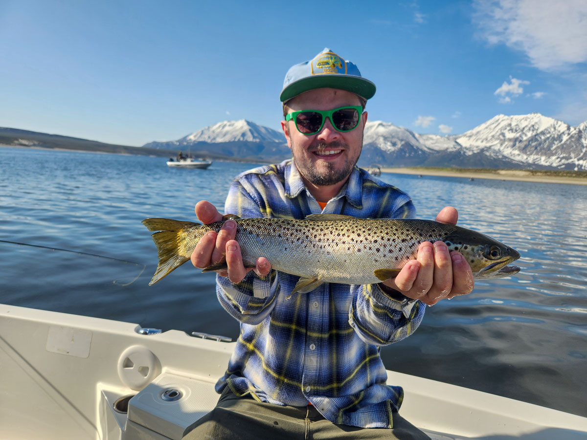 A fisherman holding a large brown trout from Crowley Lake on a boat.