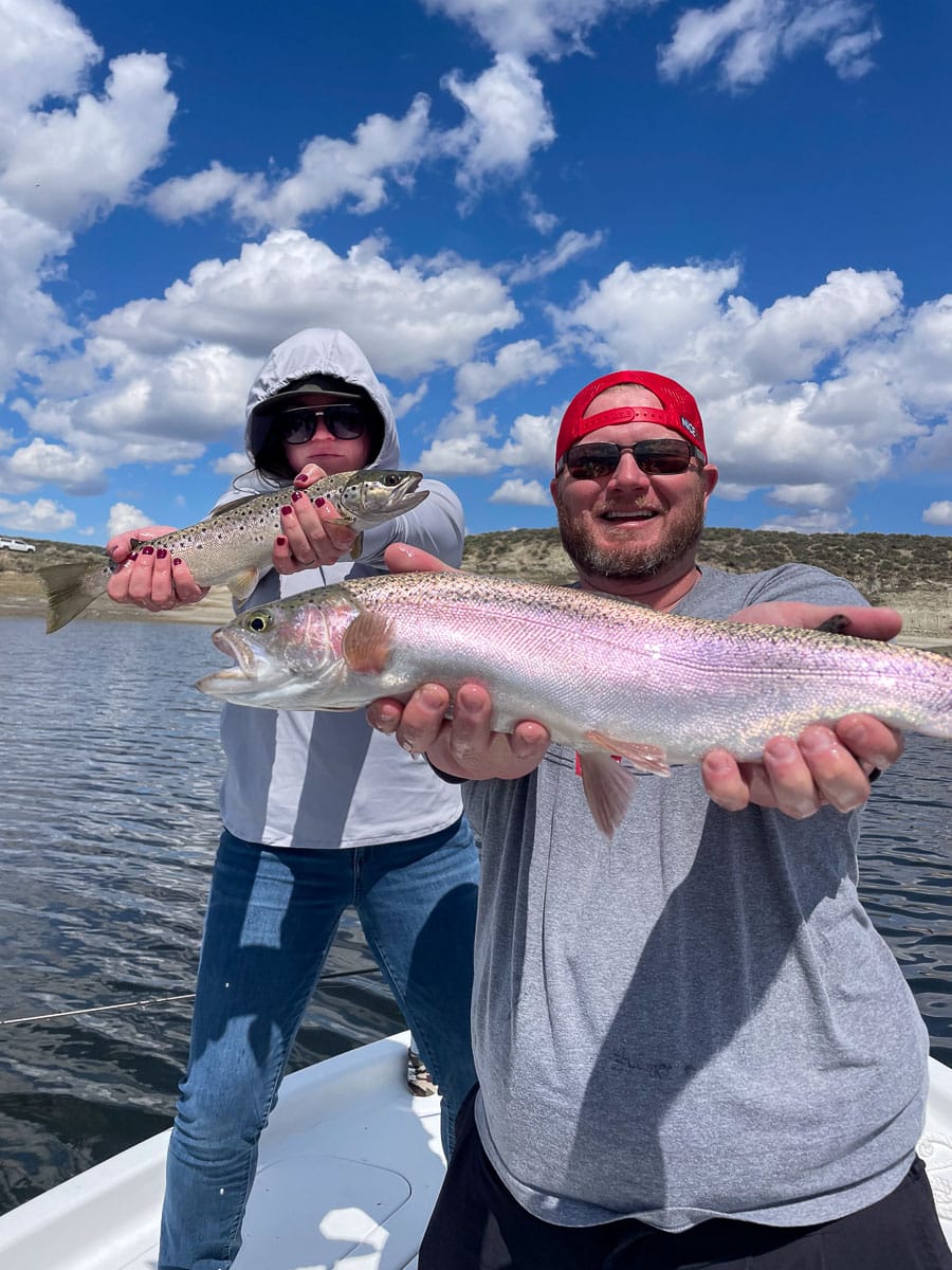 A man and a hooded woman holding a rainbow and a brown trout respectively on a boat on Crowley Lake.