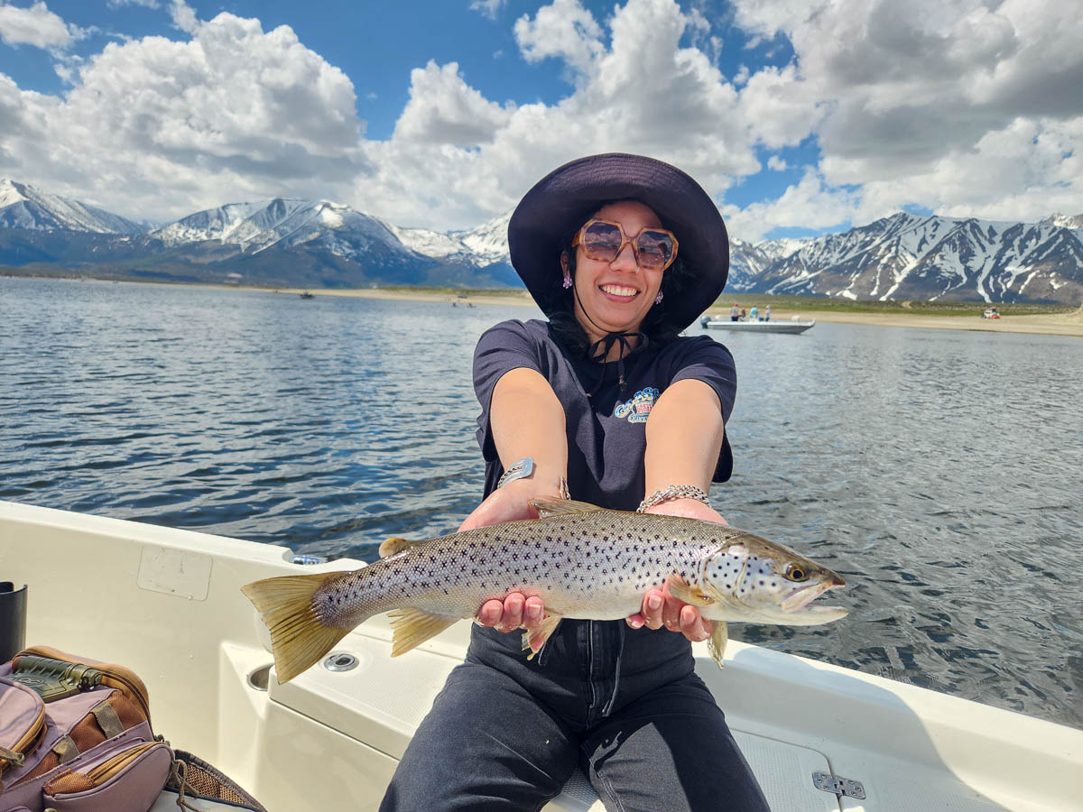 A young woman holding a large brown trout from Crowley Lake on a boat.