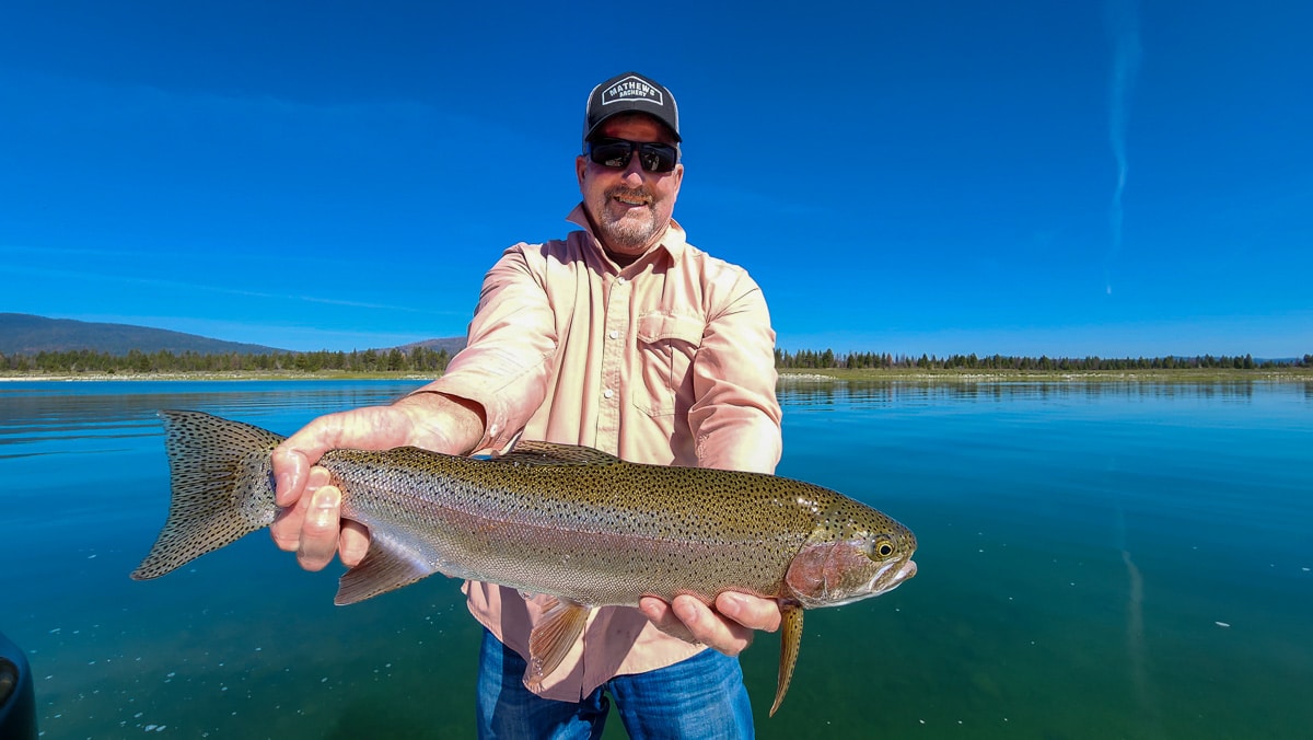 A fisherman holding a large rainbow trout from Eagle Lake on a boat.