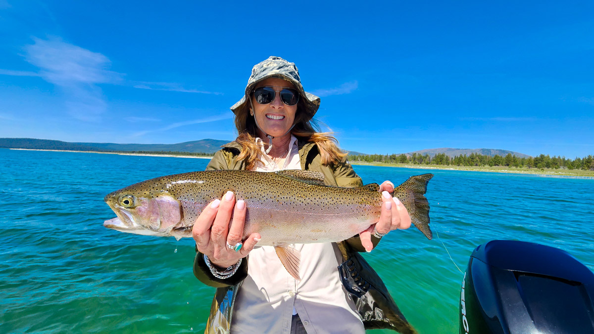 A woman holding a large rainbow trout from Eagle Lake on a boat.