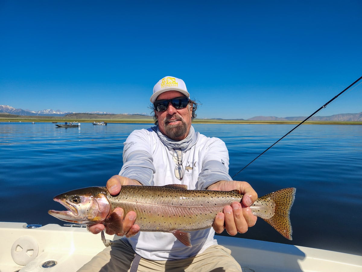 A fisherman holding a large cutthroat trout from Crowley Lake on a boat.