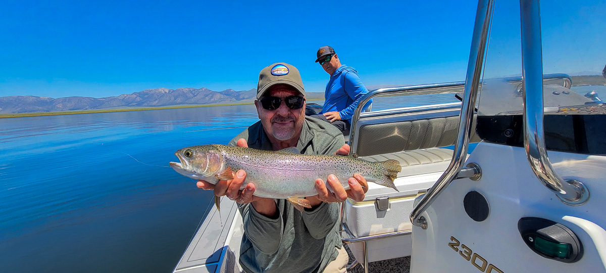 A fisherman holding a large rainbow trout from Crowley Lake on a boat.