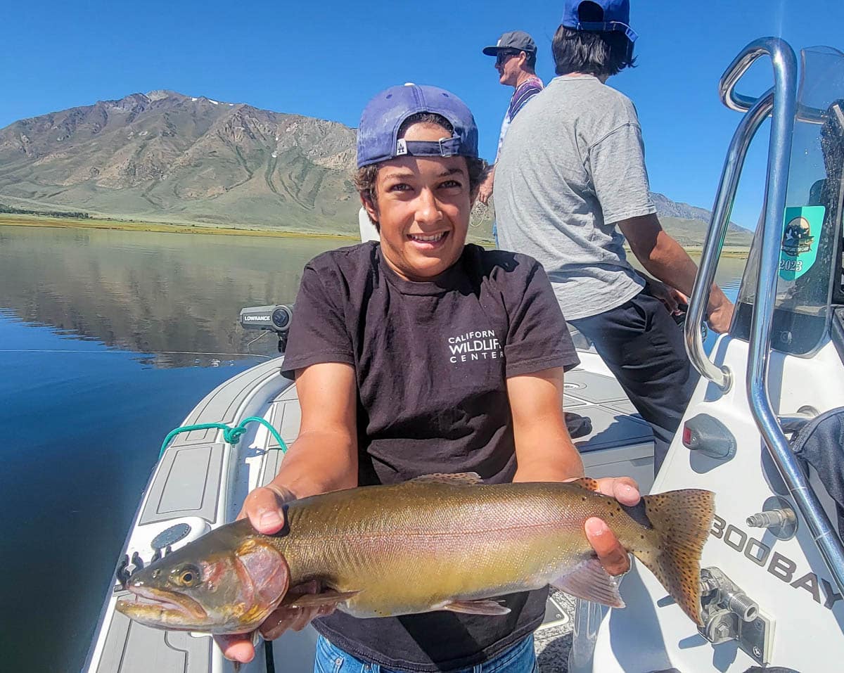 A fisherman holding a large cutthroat trout from Crowley Lake on a boat.