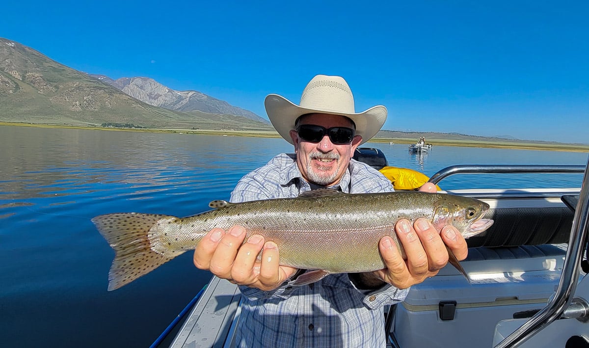 A fisherman holding a large cutthroat trout from Crowley Lake on a boat.