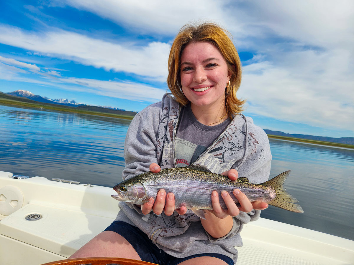 A young lady holding a rainbow trout from Crowley Lake in a boat.