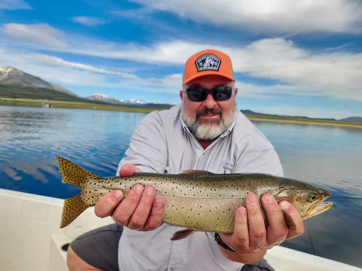 A fisherman holding a large cutthroat trout from Crowley Lake on a boat.