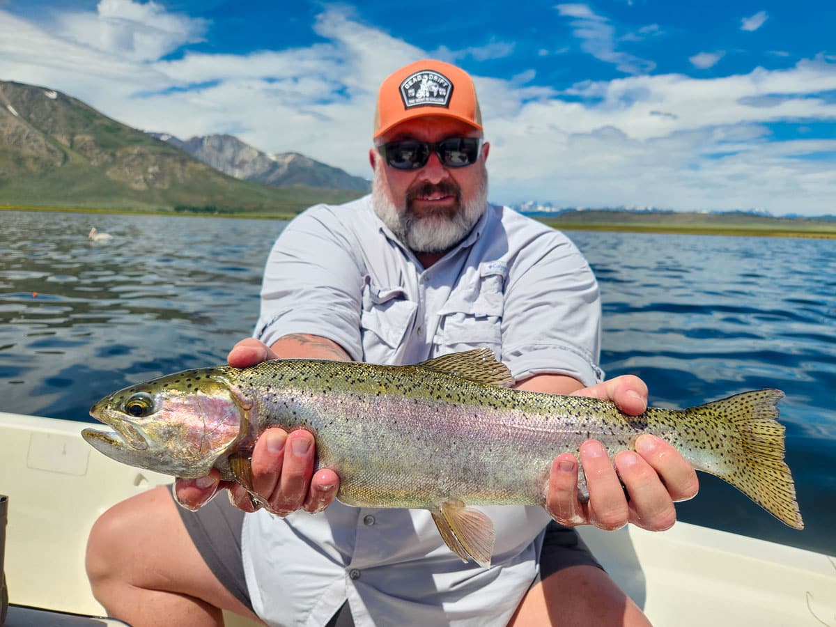 A fisherman holding a large rainbow trout from Crowley Lake on a boat.